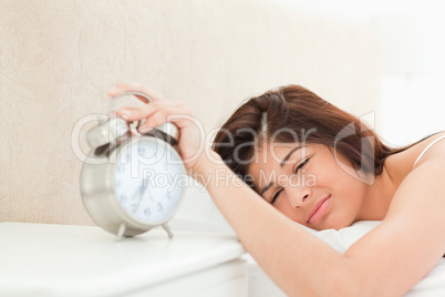 Woman silencing the ringing bell of the alarm clock with her han