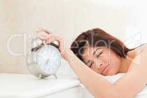 Woman silencing the ringing bell of the alarm clock with her han