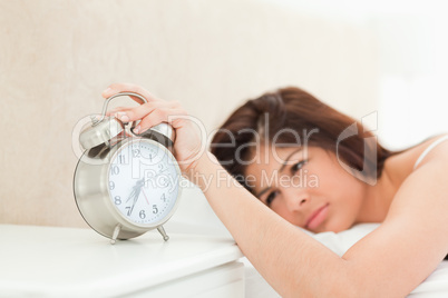An alarm clock showing the time, being silenced by a woman lying