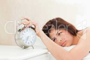 An alarm clock showing the time, being silenced by a woman lying