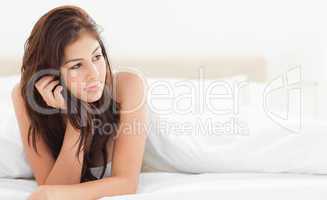 Woman lying at the end of the bed while looking to the side