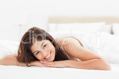 Woman lying on the bed, looking forward and smiling with her hea