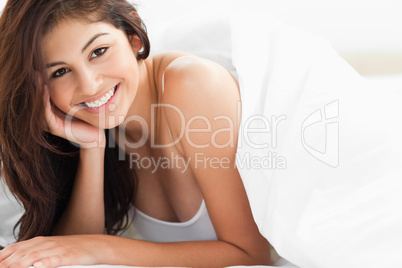 Woman lying under a quilt smiling with a hand against her cheek