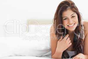 Woman lying at the bottom of the bed smiling, with her hand upon
