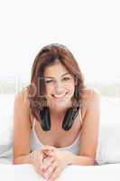 Woman on the bed looking straight ahead with headphones and smil
