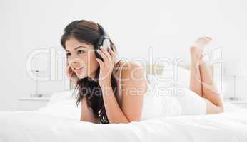 Woman lying on her bed with headphones on, listening to music wh