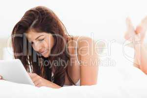 Woman using a tablet while crossing her legs on the bed