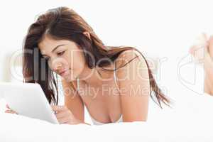 Woman lying with crossed legs on a bed while using a tablet pc