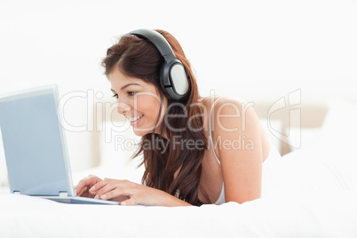 Woman browsing her laptop with headphones while lying on a bed