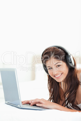 Close up, woman with headphones and a laptop lying on a bed