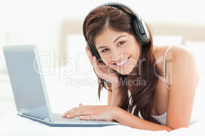 Woman lying on a bed using a laptop and listening to headphones