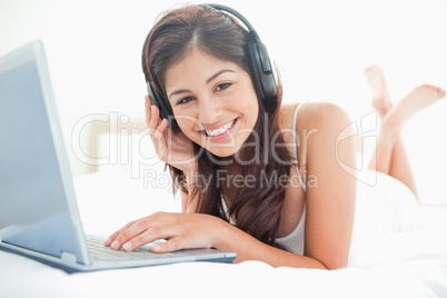 Woman looking ahead smiling, while using a laptop and headphones