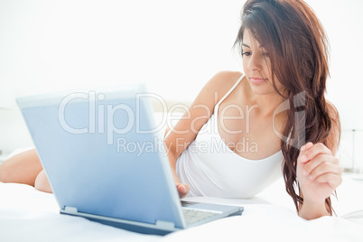 Woman lying upward across the bed while using her laptop