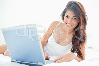 Woman lying across the bed, with her laptop beside her, and smil