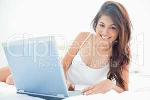 Woman lying across the bed, with her laptop beside her, and smil