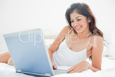 Woman relaxing across the bed with her laptop, enjoying what she