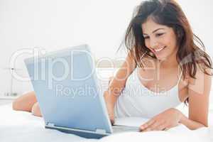 Woman lying across her bed, using her laptop and enjoying what s