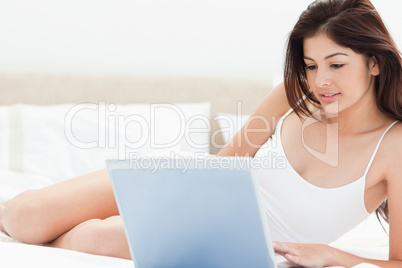 Woman lying on her bed in front of her laptop and browsing as sh