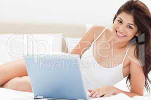 Woman looking forward and smiling as she uses her laptop on the