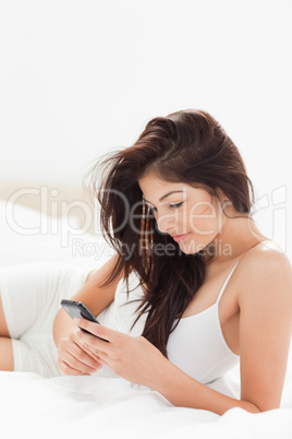 Close up, woman using her smartphone as she lies on her bed