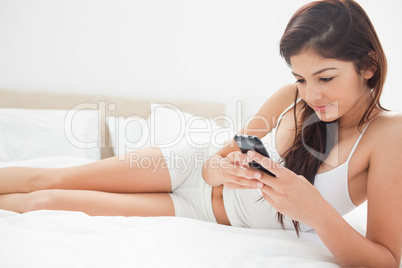 Woman focusing on her smartphone as she relaxs on the bed