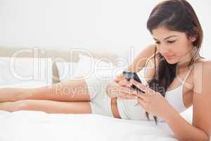 Woman focusing on her smartphone as she relaxs on the bed