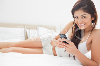 Woman lying on her bed smiling as she uses her smartphone