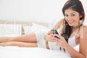 Woman lying on her bed smiling as she uses her smartphone