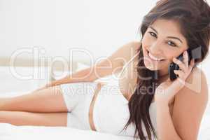 Woman using her smartphone and smiling while lying on her bed