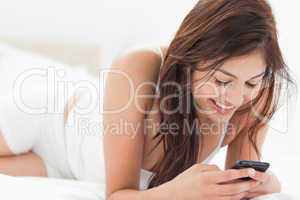 Woman smiles as she uses her phone while relaxing on her bed
