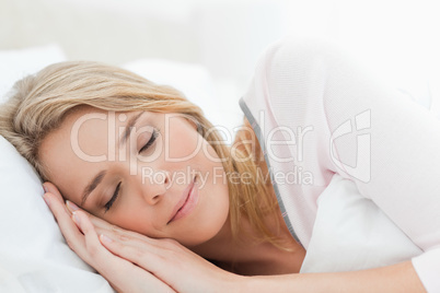 Woman sleeping in bed, her head resting on a pillow and hands be