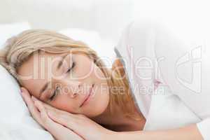 Woman sleeping in bed, her head resting on a pillow and hands be