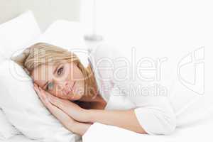 Horizontal shot, woman resting in bed, eyes open with hands and