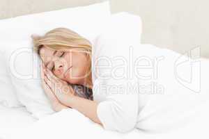 Woman sleeping in bed with hands placed beside her head on the p