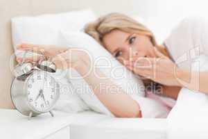 Woman waking up, yawning nd reaching over to silence alarm clock