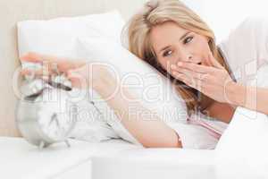 Woman yawning while she reaches out to silence her alarm clock