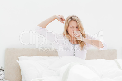 Woman sitting upright in bed, stretching her arms as she wakes u