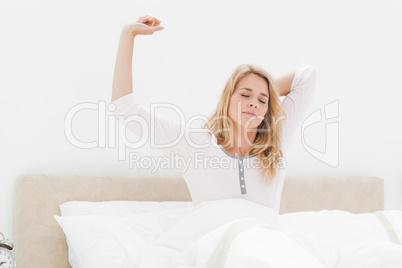 Woman upright in bed stretching with arm raised and eyes closed