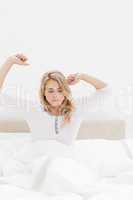 Closer shot of woman in bed sitting up with stretched out arms