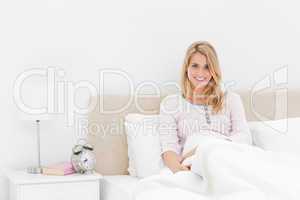 Woman leaning up against the headboard, smiling with the alarm c