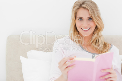 Woman holding her book in hand, while in bed looking forward and