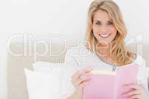 Woman holding her book in hand, while in bed looking forward and