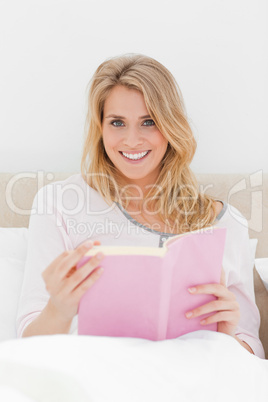 Close up shot, Woman sitting in bed, book in hand as she looks f