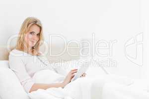Woman in bed, sitting up with a tablet pc in hand, looking to th