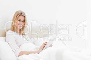 Woman sitting in bed, with tablet pc in hand, looking up and smi