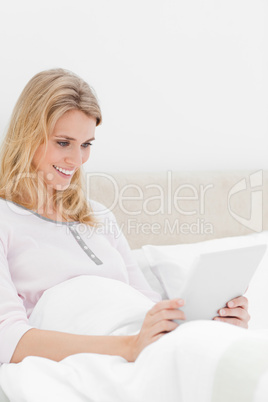 Woman sitting in bed, holding a tablet with both hands, and smil