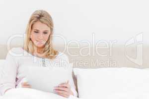 Woman sitting in bed, holding and watching a tablet pc