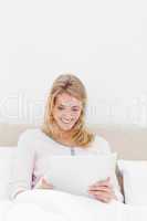 Centered shot, woman sitting in bed watching tablet pc and smili