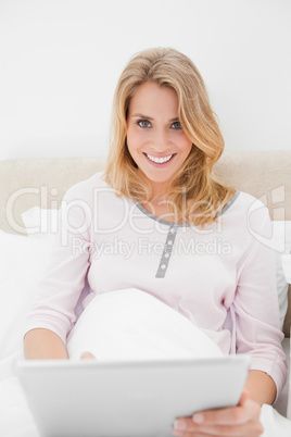Woman looking forward and smiling as she uses a tablet pc in bed