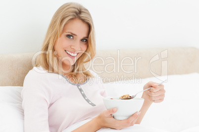 Woman in bed with a bowl of cereal in hand and a slightly raised